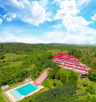 Un hotel grande con techo rojo, piscina y edificio de color rojo y blanco.
