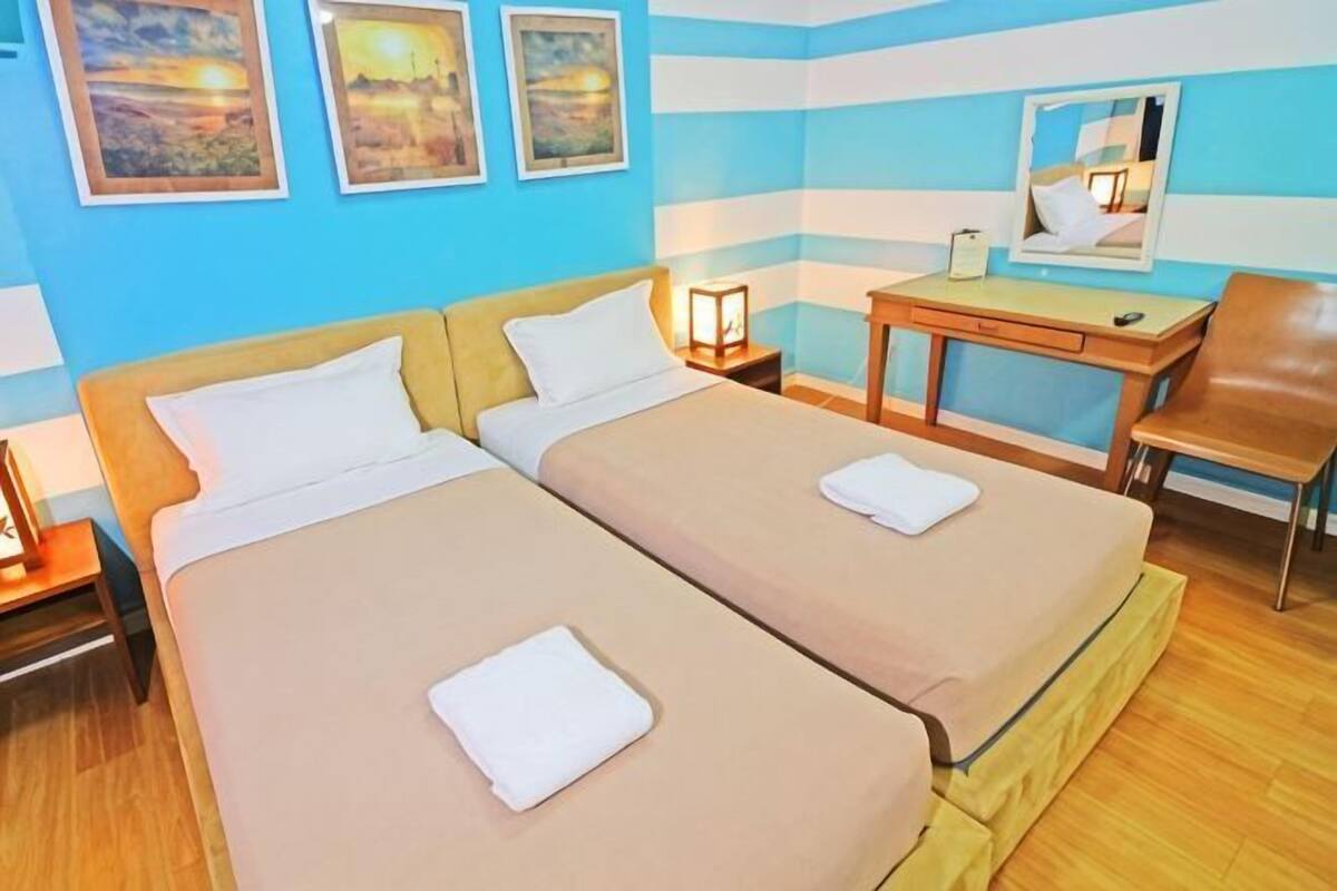 A hotel room with two beds, a desk, a chair, and artwork on the walls.