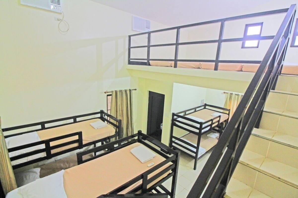 A dormitory-style room with bunk beds, a staircase, and a window.