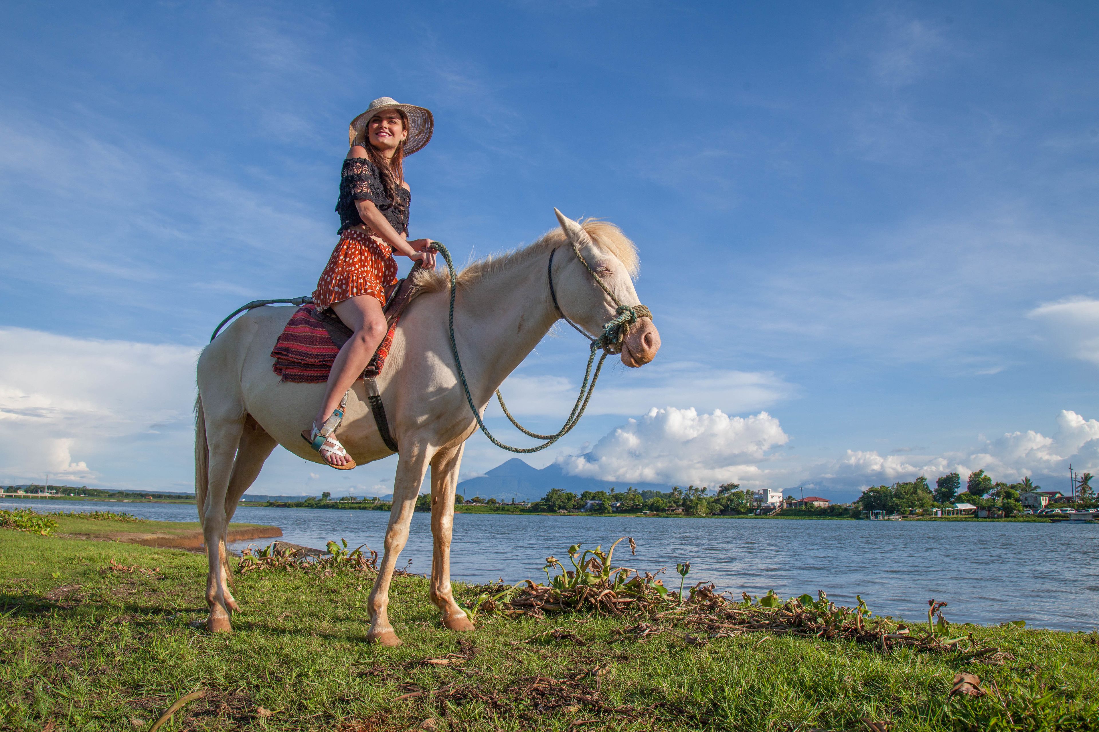 A person riding a horse by a lake with a mountain in the background.