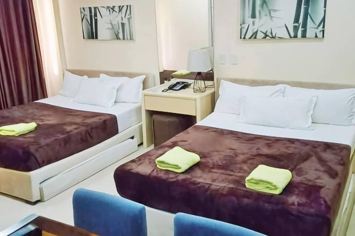 A hotel room with two beds, a desk, a chair, and artwork on the walls.