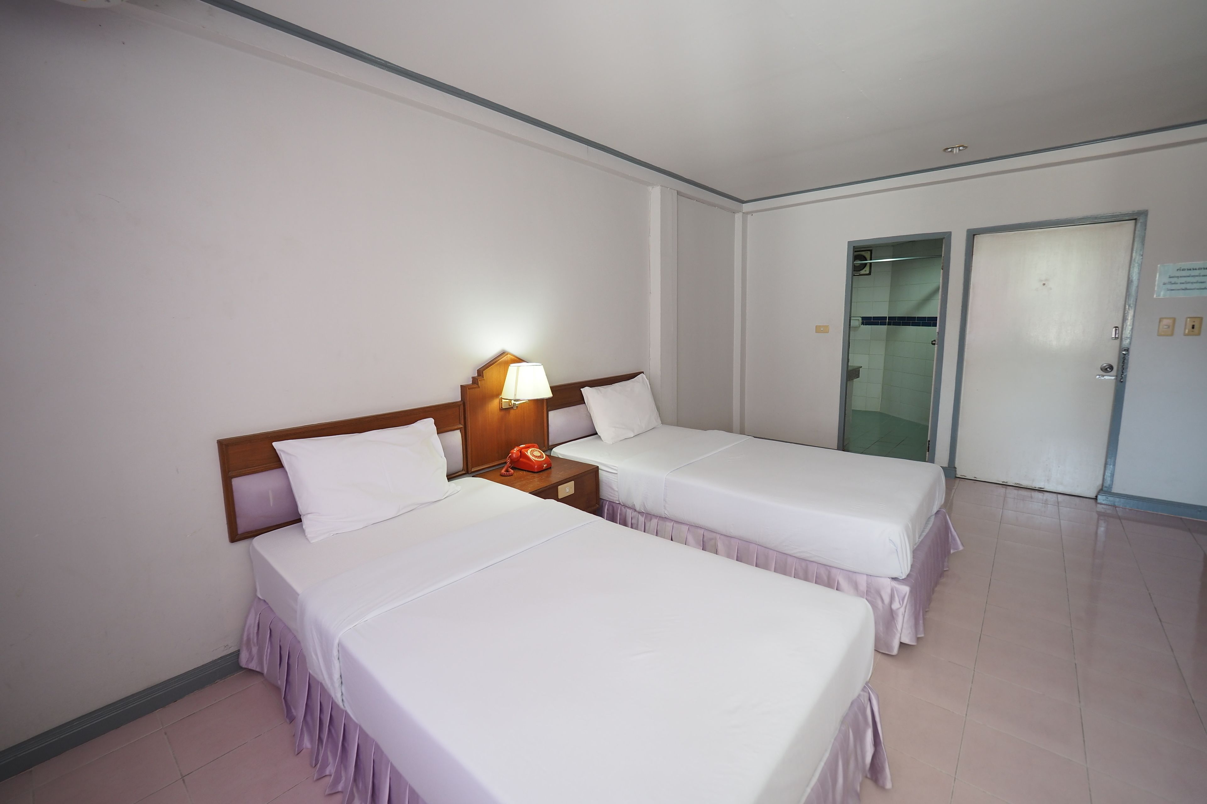 Habitación de hotel con dos camas, una mesita de noche con lámpara y una puerta que da a un baño.