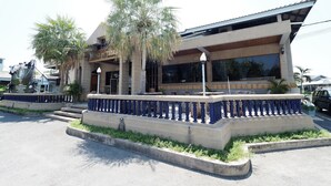 A building with a modern architectural style, featuring a balcony with blue balustrades and a concrete base. - Pachara Hotel and Restaurant (Suphan Buri)