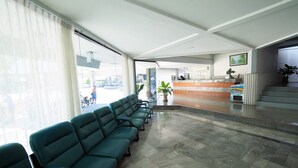 A hotel lobby with a reception desk, a waiting area with chairs, and a large window. - Pachara Hotel and Restaurant (Suphan Buri)