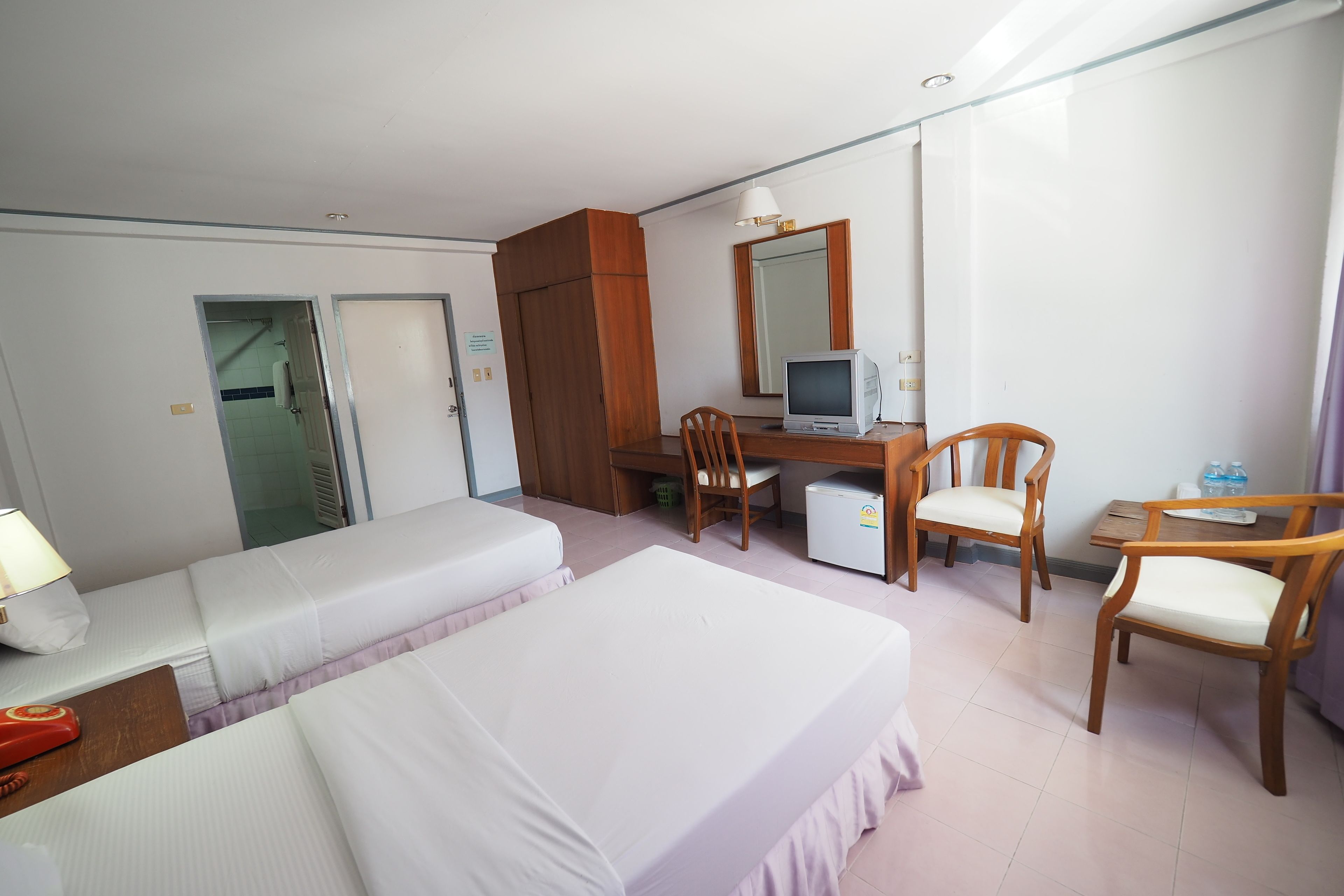 Habitación de hotel con dos camas, un escritorio con computadora, una silla y un refrigerador pequeño.