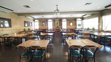 A spacious dining area with multiple tables and chairs, large windows, and a chandelier.