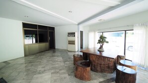 A spacious room with a large wooden dining table, two wooden stools, and a potted plant. - Pachara Hotel and Restaurant (Suphan Buri)