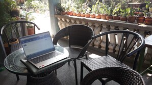 Un ordinateur portable est posé sur une table en verre, entouré de chaises en osier et de plantes en pot.