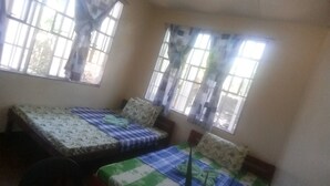 Une chambre avec deux lits, chacun agrémenté de draps à motifs. Elle est dotée de fenêtres avec des rideaux et présente un aménagement simple et fonctionnel.