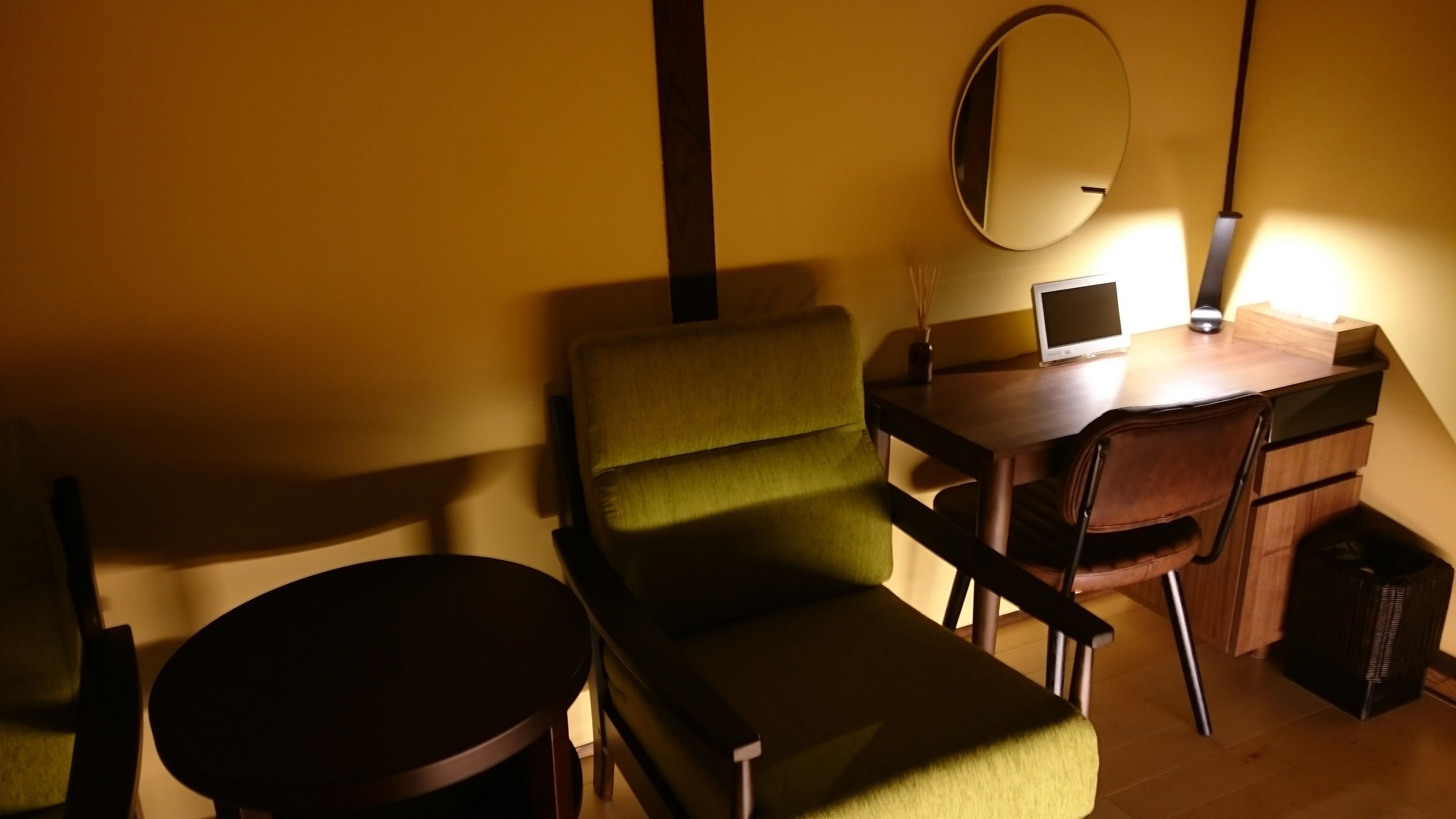 A room with a green chair, a wooden desk, a laptop, and a small round table.