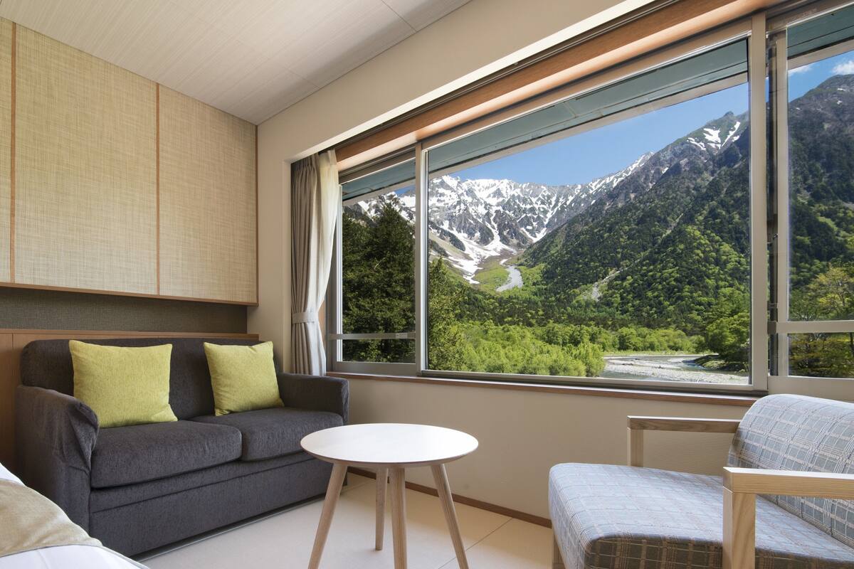 A modern room with a sofa, a small round table, and a view of a mountainous landscape through a large window.