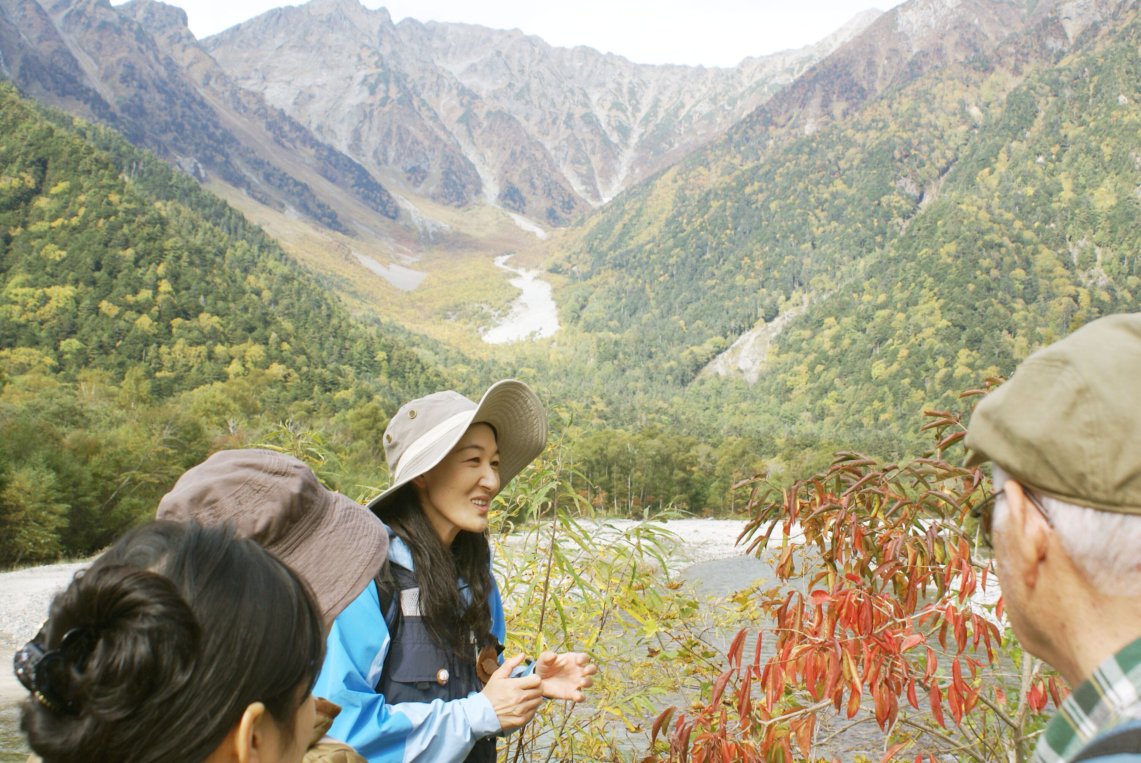 A group of people standing by a river with mountains in the background.