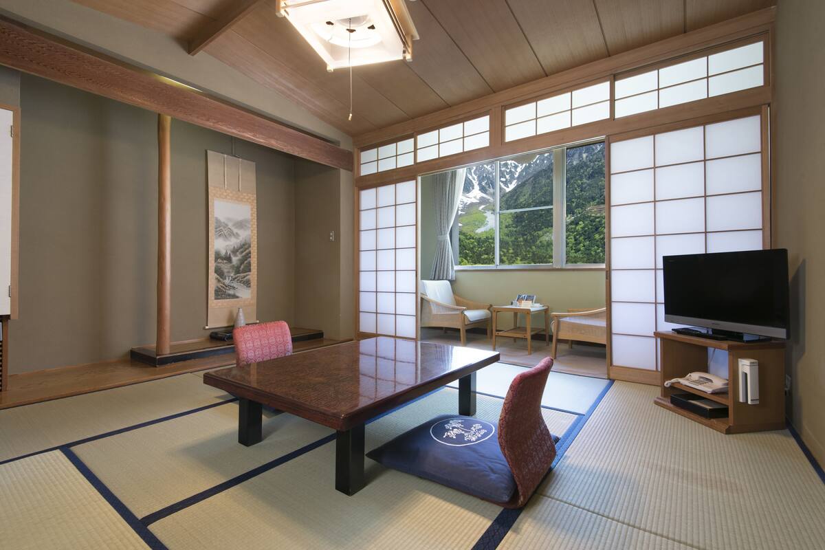 A traditional Japanese room with tatami flooring, a low table, and a television on a wooden stand.