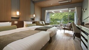A hotel room with two beds, a desk, a chair, and a large window with a view of greenery.