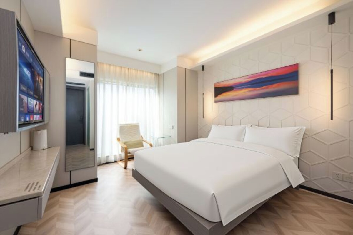 A modern hotel room with a large bed, a flat-screen TV, a seating area, and a painting on the wall.