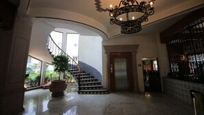 A grand lobby with a curved staircase, a chandelier, and a potted plant.
