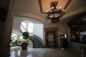 Un amplio vestíbulo con una escalera curva, un candelabro y una planta en maceta.