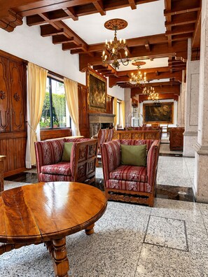Ein geräumiges Zimmer mit Holzbalkendecke, einem großen runden Tisch und gestreiften Sofas.