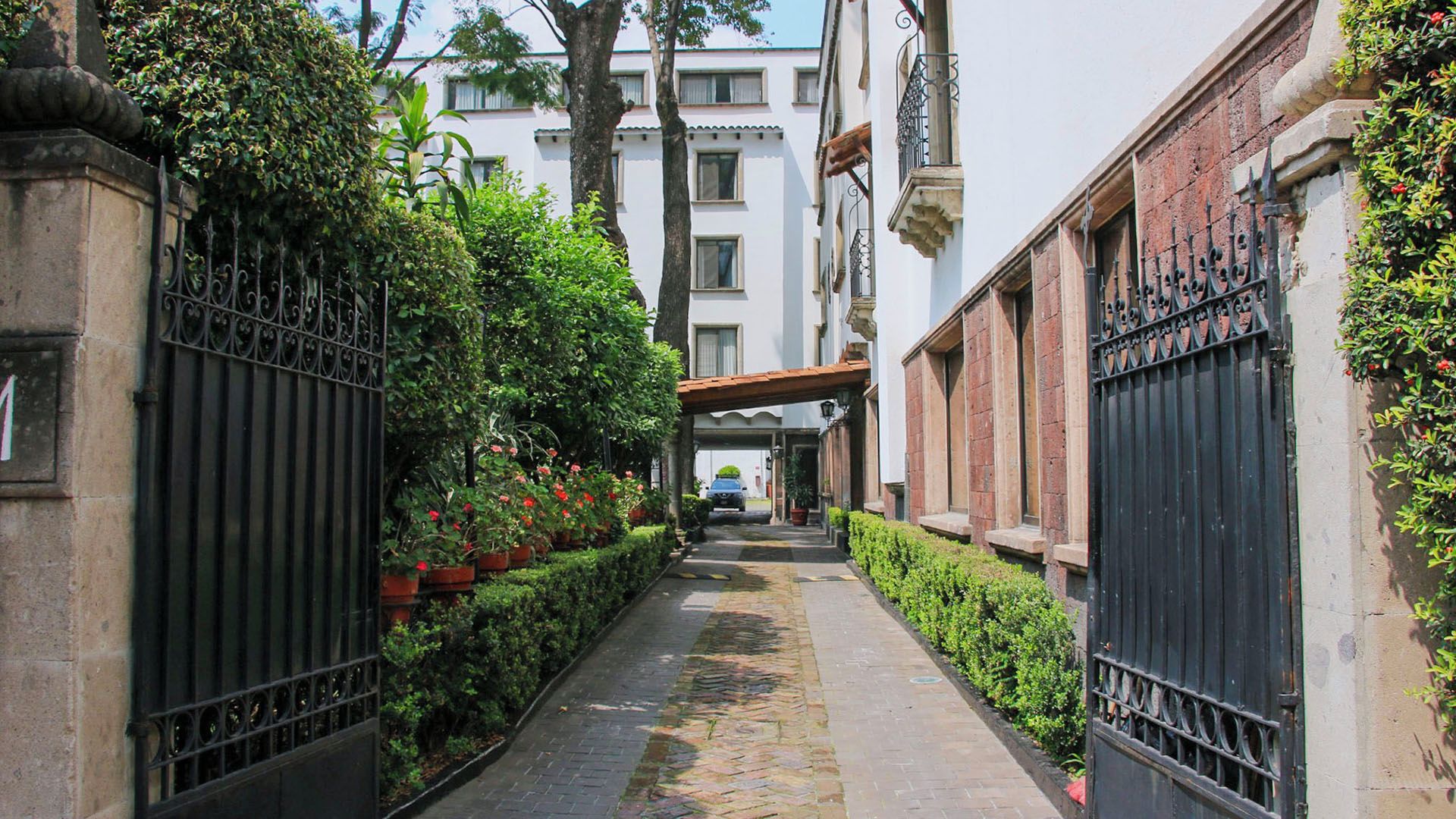 Un estrecho callejón con un sendero empedrado, flanqueado por edificios con portones de hierro y abundante vegetación.