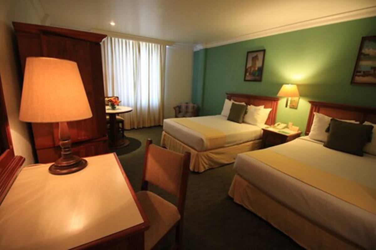 A hotel room with two beds, a desk, a chair, a lamp, a nightstand, and a window with curtains.