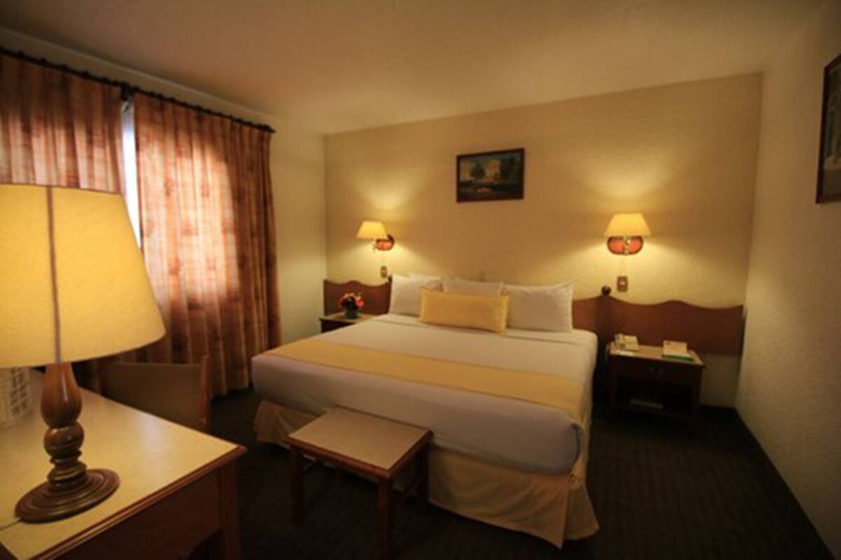 A hotel room with a bed, two bedside tables, a desk with a lamp, a chair, and a small table.