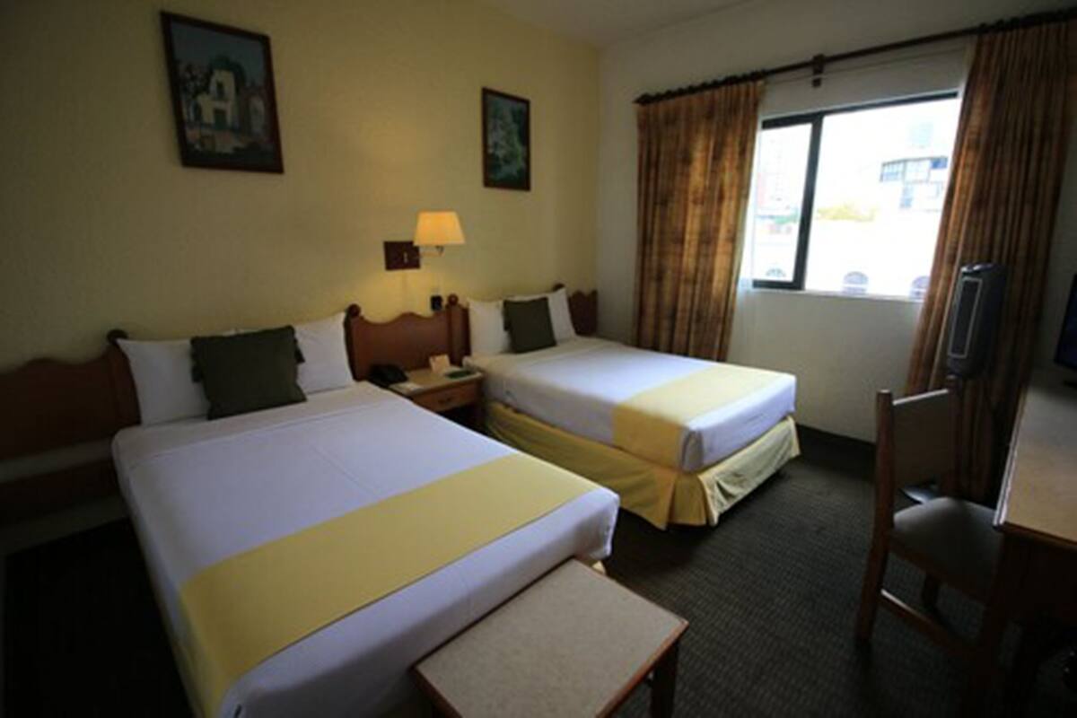 A hotel room with two beds, a desk, a chair, a lamp, and a window with curtains.