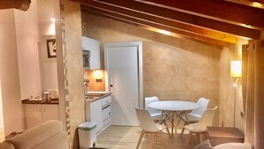A compact room with a bed, a small kitchenette, a dining table with chairs, and a bathroom.