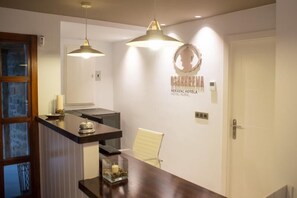 Un área de recepción con un mostrador de madera, dos lámparas colgantes, una silla blanca y un cartel en la pared para el Hotel Osabarem.