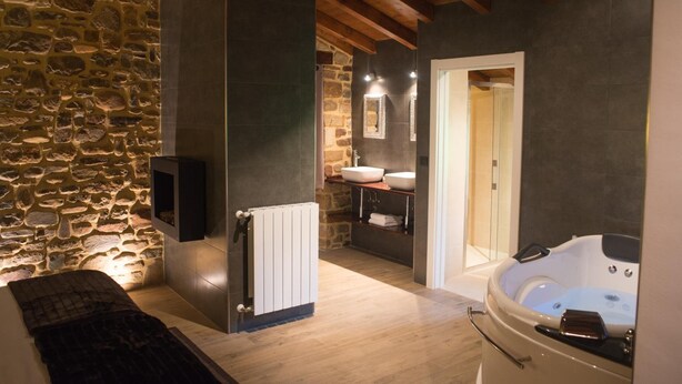 A modern bathroom with a stone wall, a white bathtub, and a wooden floor.