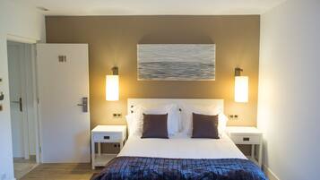 A hotel room with a large bed, two bedside tables, a wall-mounted artwork, and two wall sconces.