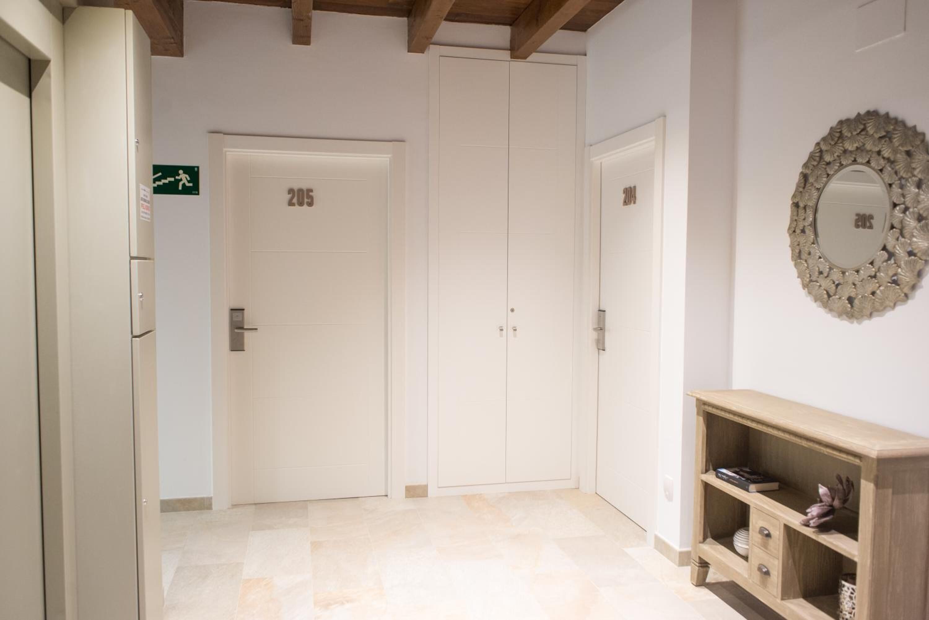 A hallway with double doors labeled 205 and 206, a wooden console table with decorative items, and a mirror on the wall.