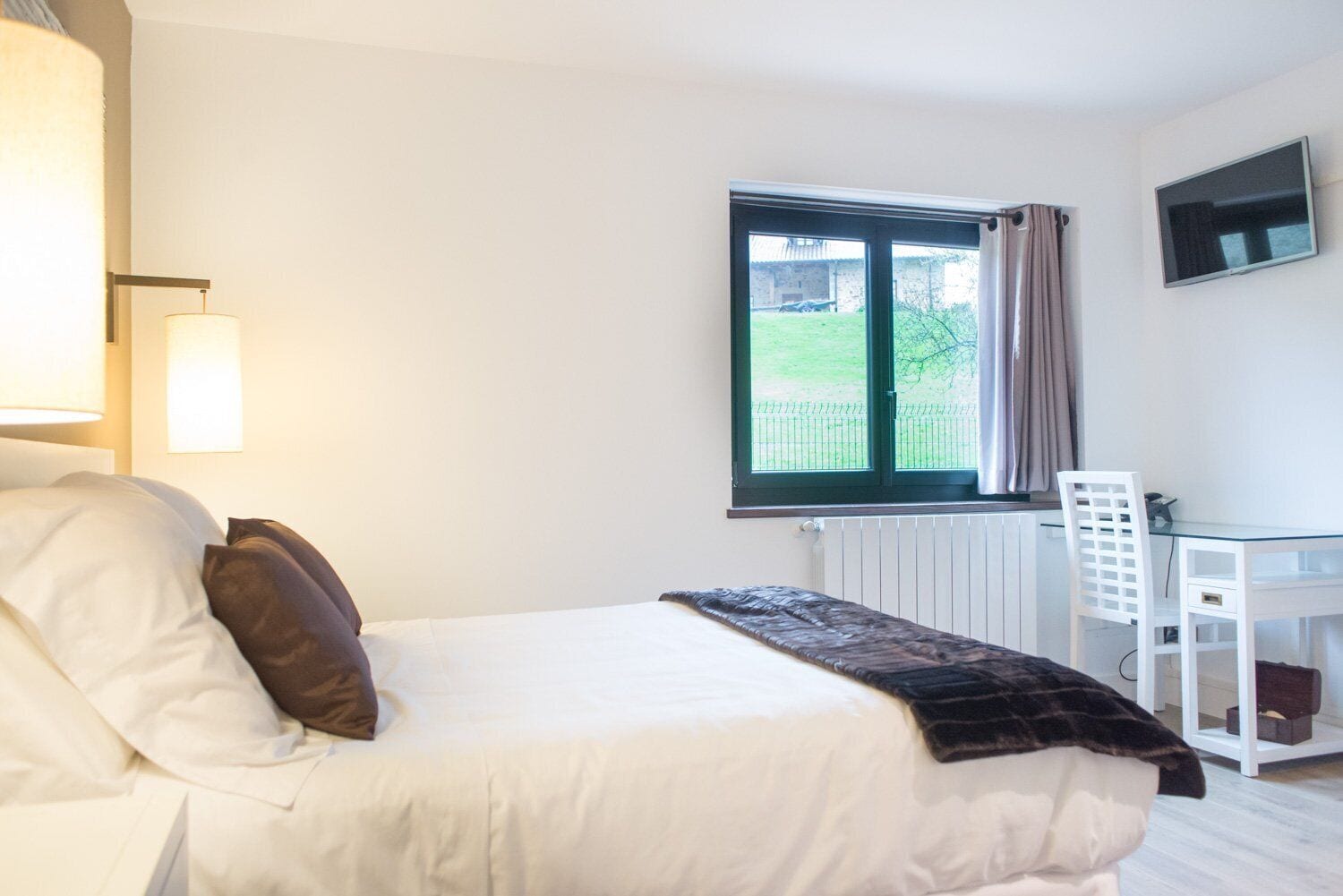 Een slaapkamer met een bed, een bureau, een stoel, een raam en een radiator.