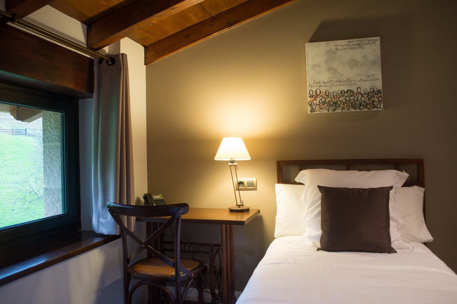 Una habitación de hotel con una cama, un escritorio con lámpara, una silla y una ventana con cortinas.