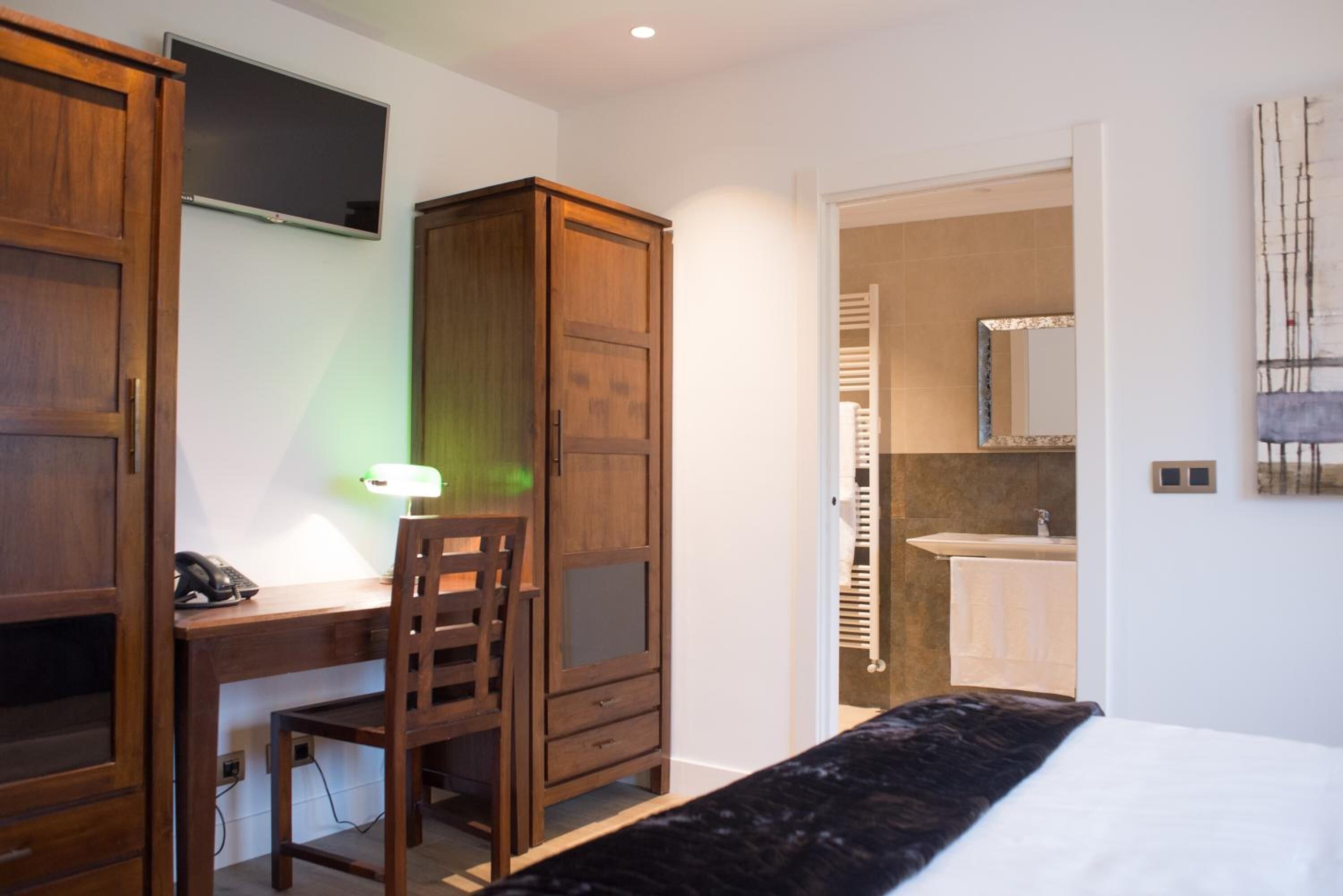 Quarto com escrivaninha de madeira, cadeira e cama com colcha preta.