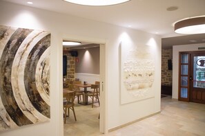 Un pasillo de hotel con una zona de comedor, una pared con arte abstracto y una puerta que dice "BARBERIA".