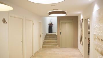 A modern hallway with a staircase leading to a door, light fixtures, and a wall with artwork.
