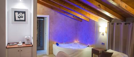 A bedroom with a large bed, a wooden ceiling, a bathtub, and a small table with a coffee maker.