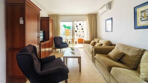 A living room with a sofa, armchairs, a coffee table, and a TV. There is a door with a lock and a window with curtains. - Apartamentos Maja Beach (Benidorm)