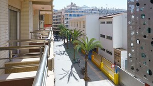 A balcony with a metal railing, a palm tree, and a building with a perforated facade. - Apartamentos Maja Beach (Benidorm)