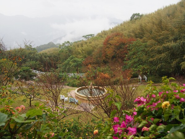 A circular water feature surrounded by a stone pathway, with a white bridge in the background and lush greenery.
