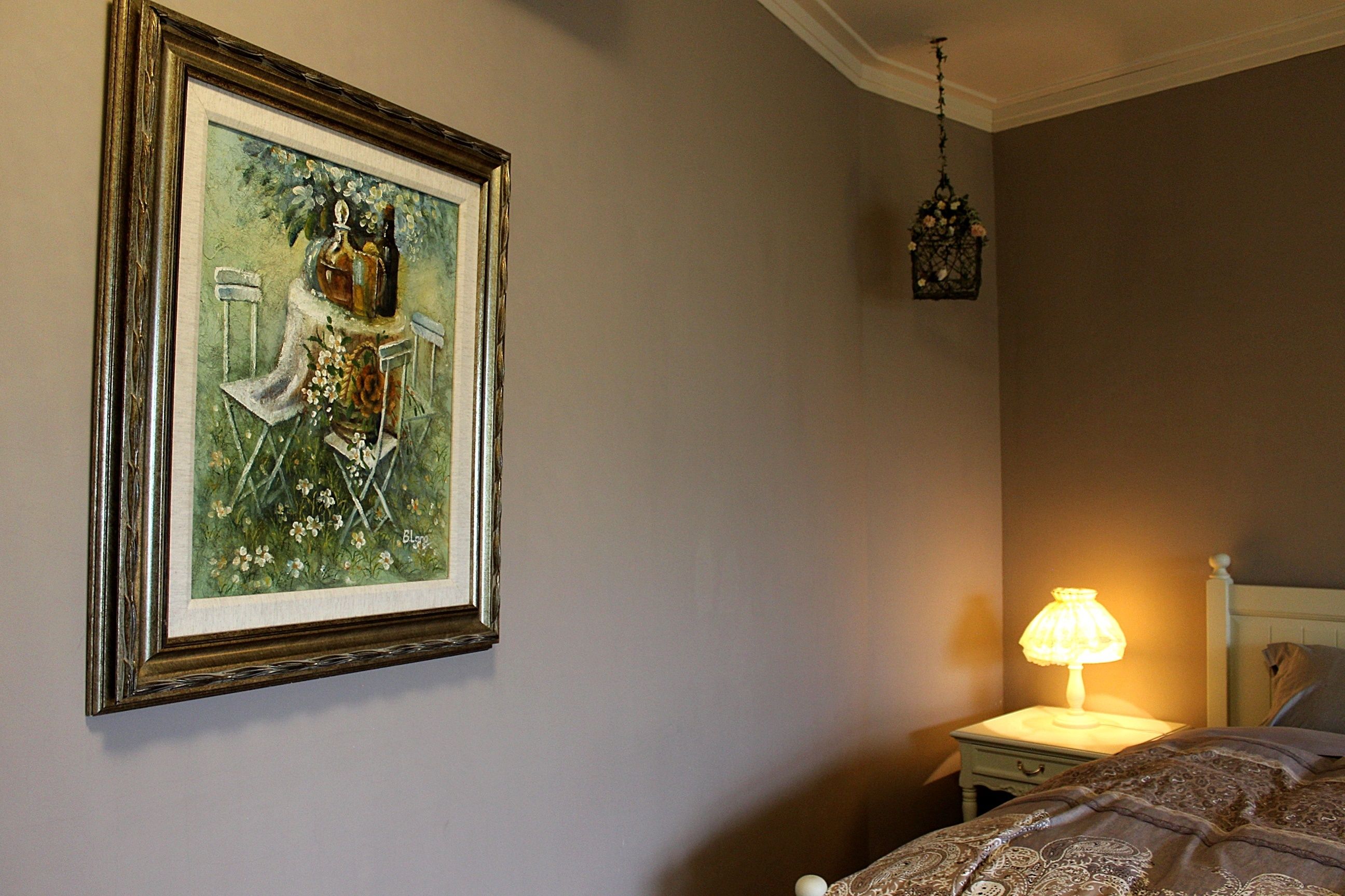 A bedroom with a framed painting, a bedside lamp, and a hanging light fixture.