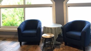 Une pièce avec deux fauteuils bleus, une petite table ronde et de grandes fenêtres en arc de cercle.
