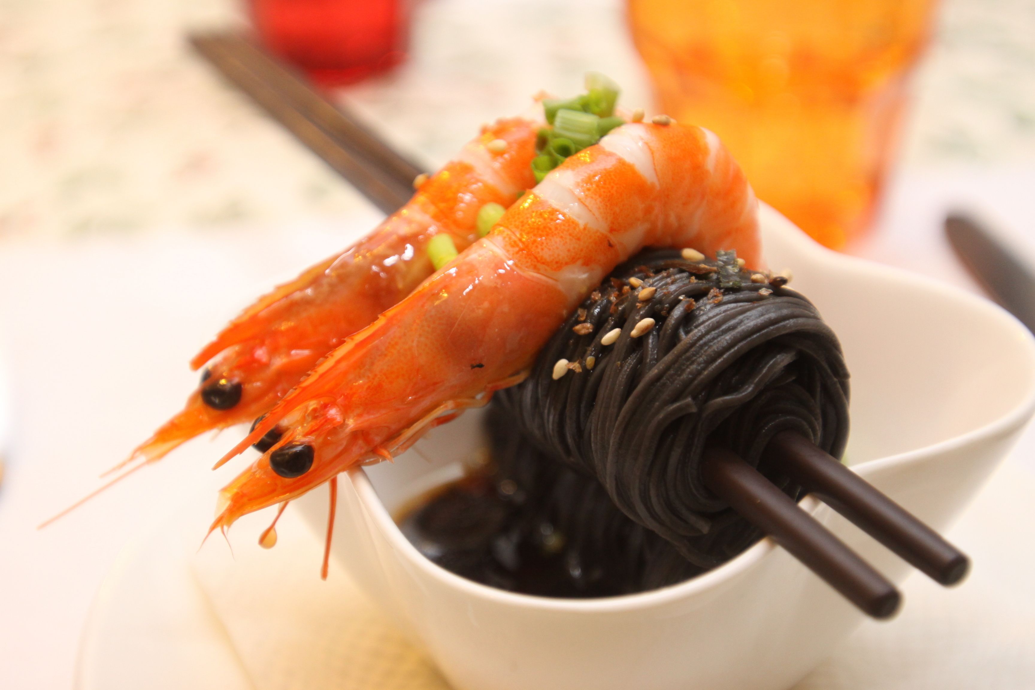 A bowl of food with two shrimp and a dark-colored item, possibly a dessert or side dish, garnished with green onions and sesame seeds.