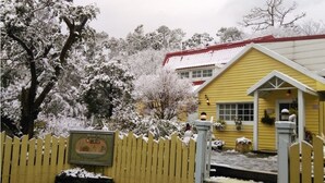 Un bâtiment jaune avec un toit rouge, entouré d’arbres couverts de neige et d’une clôture en bois.