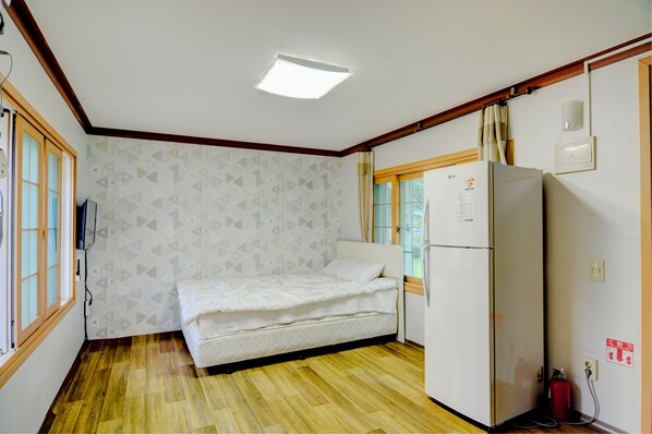 Um quarto pequeno com uma cama, um frigorífico e uma janela com cortinas.