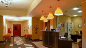 A hotel reception area with a check-in counter, orange chairs, a fire extinguisher, and a red door. - Hotel Torre del Duca (San Floro)