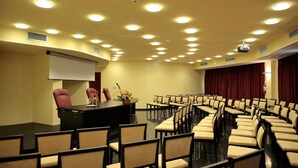 A conference room with a stage, rows of chairs, and a projector screen. - Hotel Torre del Duca (San Floro)