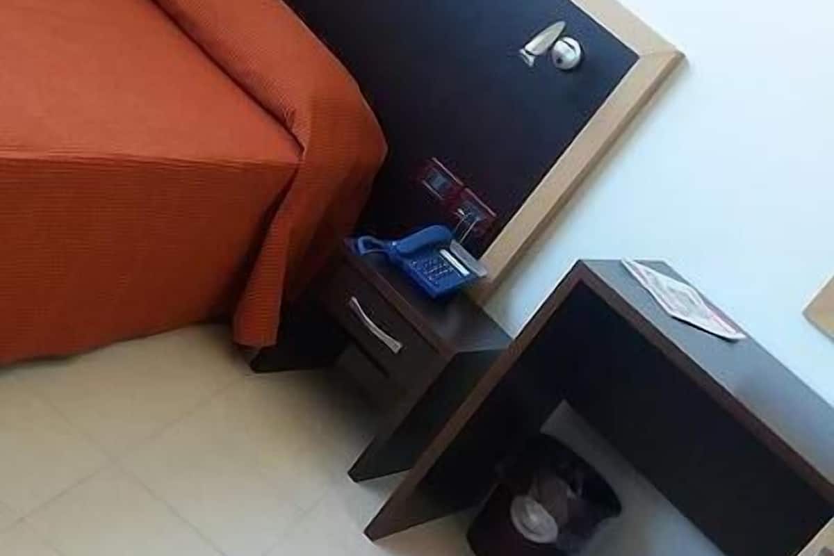 A bedroom with a bed, a nightstand, a small table, and a trash bin.