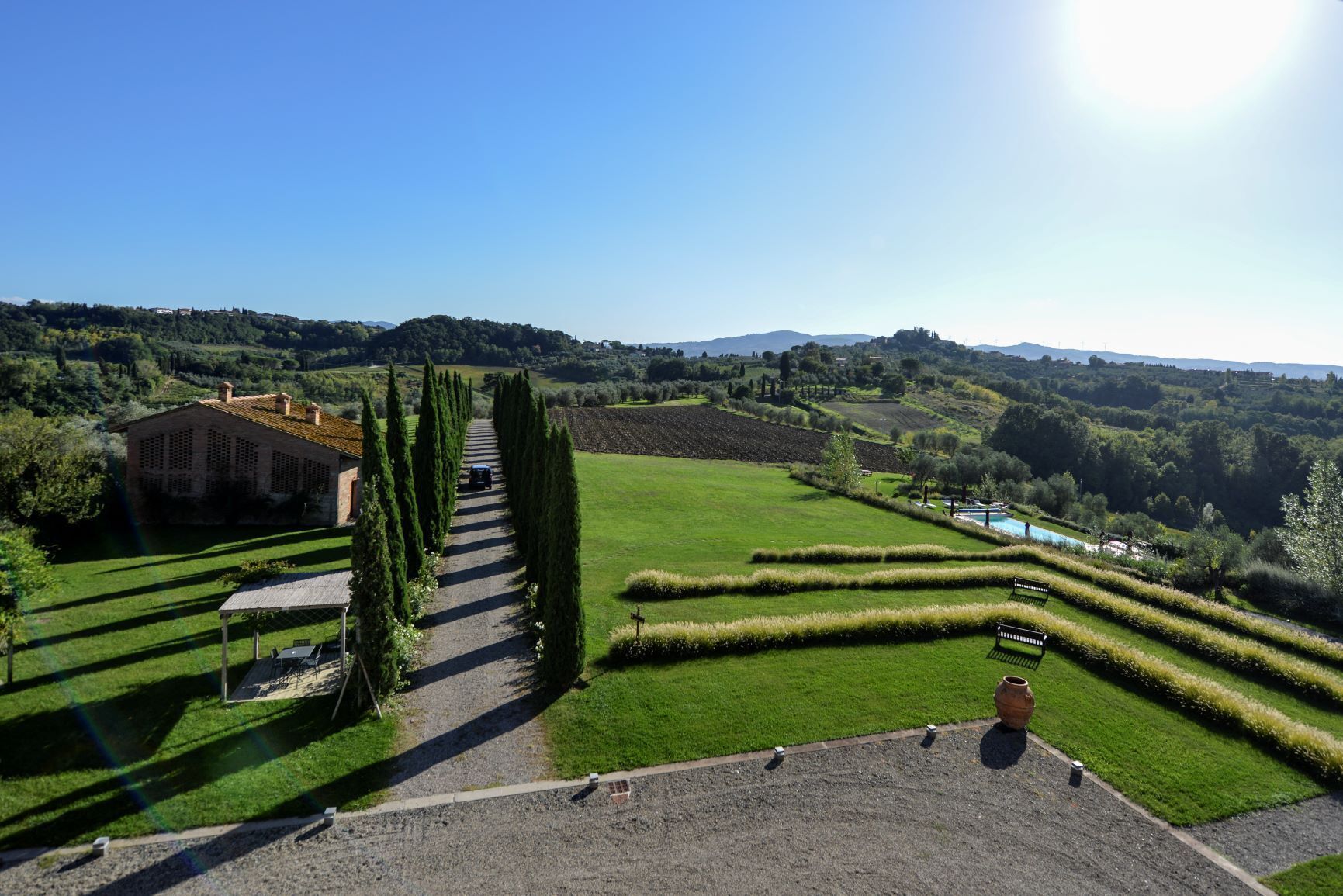 Un jardín bien cuidado con un camino de grava que lleva a un edificio, rodeado de setos ordenados y vistas despejadas del campo.