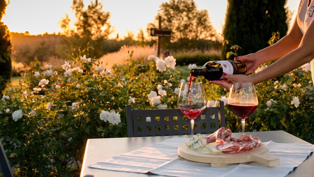Une table avec une bouteille de vin, deux verres et une assiette de fromage et de charcuterie.